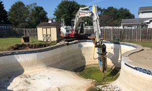 Takeuchi Excavator with a hydraulic breaker being used to remove pool
