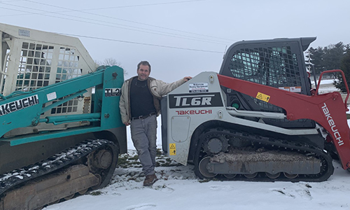 Thomas Jackson standing in between two Takeuchi Track Loaders